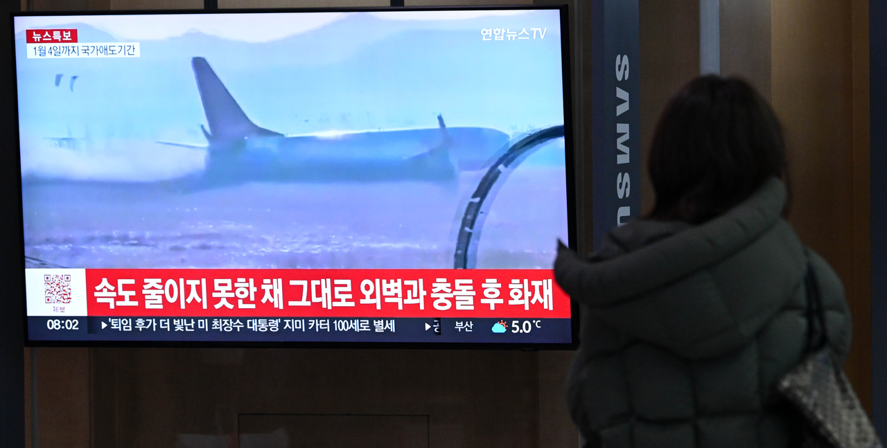 A passerby watches a news broadcast about the crash of a Jeju Air aircraft, at Seoul Station on Monday. (Im Se-jun/The Korea Herald)