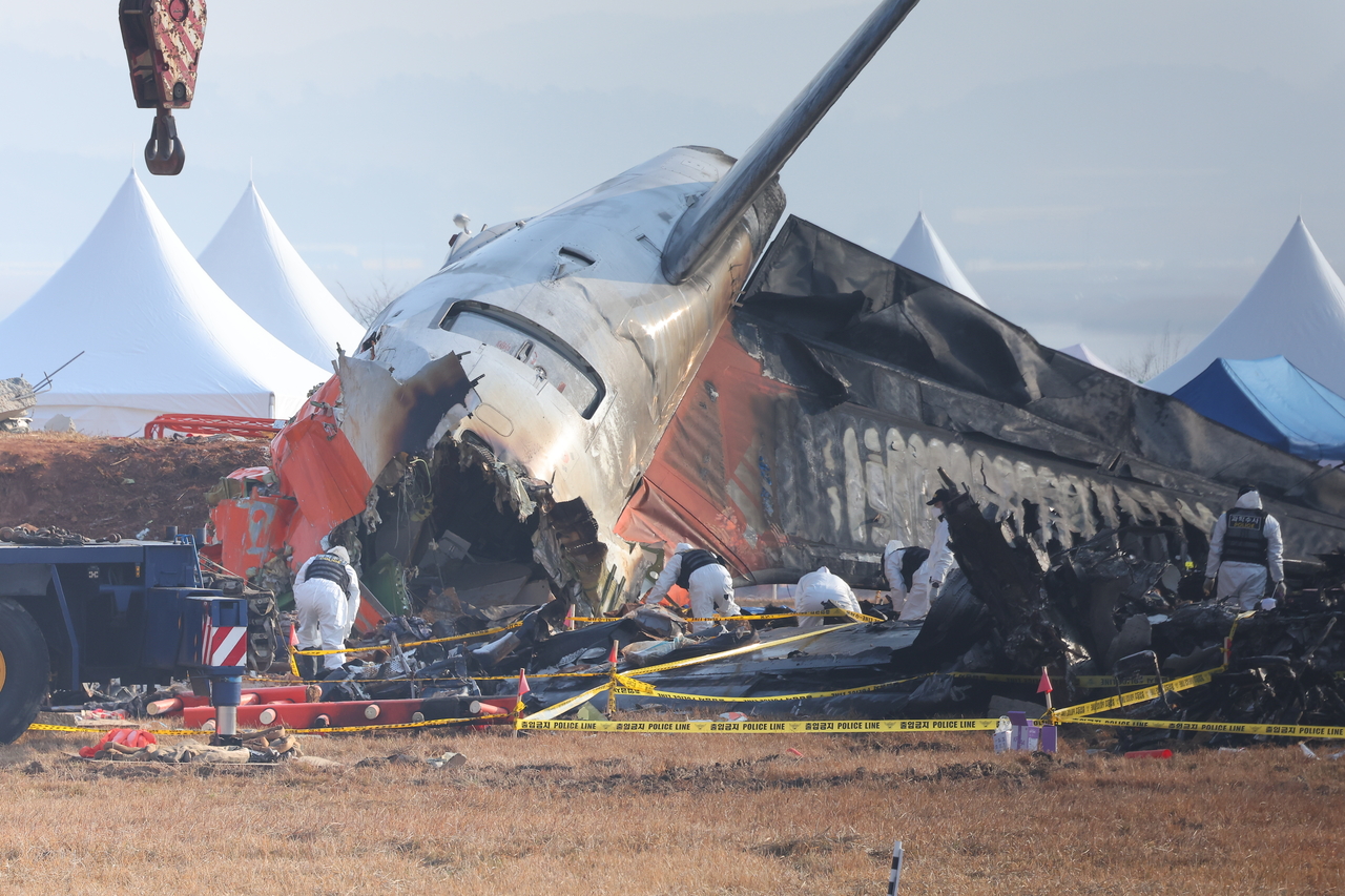 Police investigators search the Jeju Air plane that belly-landed and crashed into a barrier, killing 179 passengers aboard and leaving only two survivors, on Thursday. (Yonhap)
