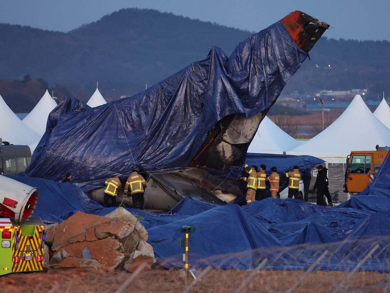 Firefighters cover the tail wing of the wrecked Jeju Air plane with a tarp at the crash site at Muan International Airport in Muan County, South Jeolla Province, on Saturday after the search operation ended. (Yonhap)