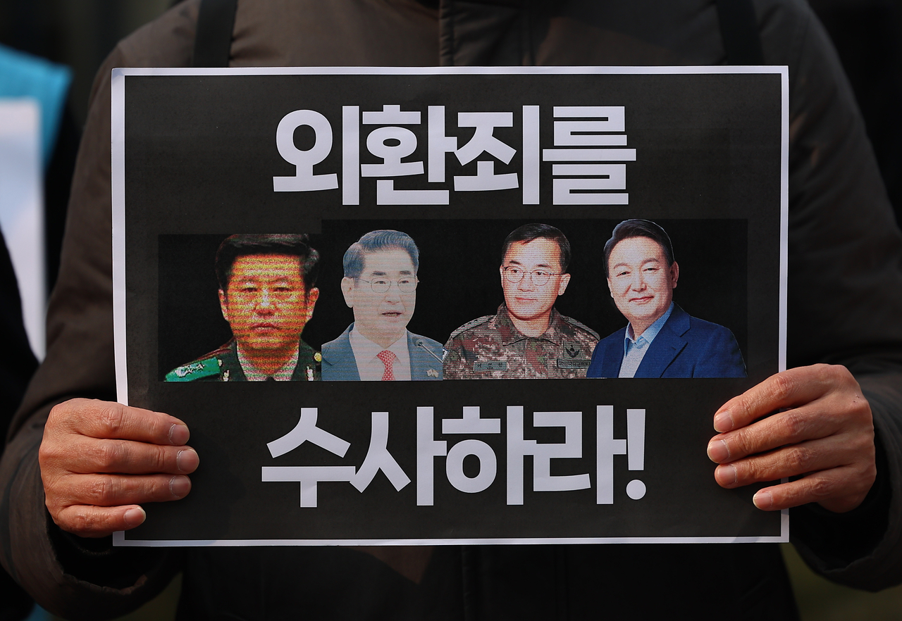A protestor holds a sign with pictures of former Defense Minister Kim Yong-hyun, Lt. Gen. Yeo In-hyung, head of the Defense Counterintelligence Command and President Yoon Suk Yeol at a press briefing calling for an investigation launch for treason in front of the National Police Agency in Seodaemun, Seoul. (Yonhap)