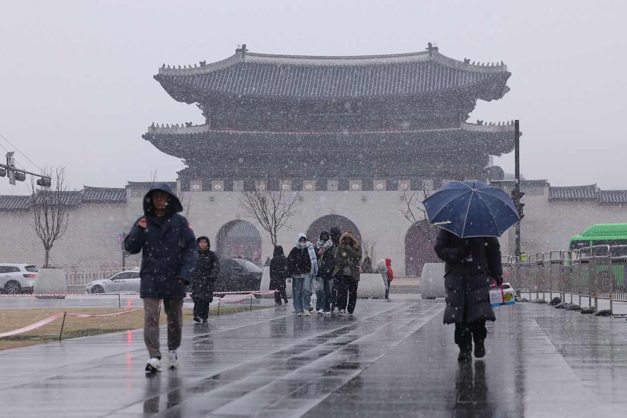 Pedestrians wait to cross the street as snow falls near Gwanghwamun Square in Seoul on Jan. 13. (Yonhap)