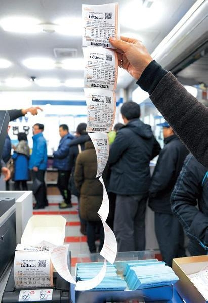 A  Seoul lottery shop clerk holds up Lotto tickets. (The Korea Herald)