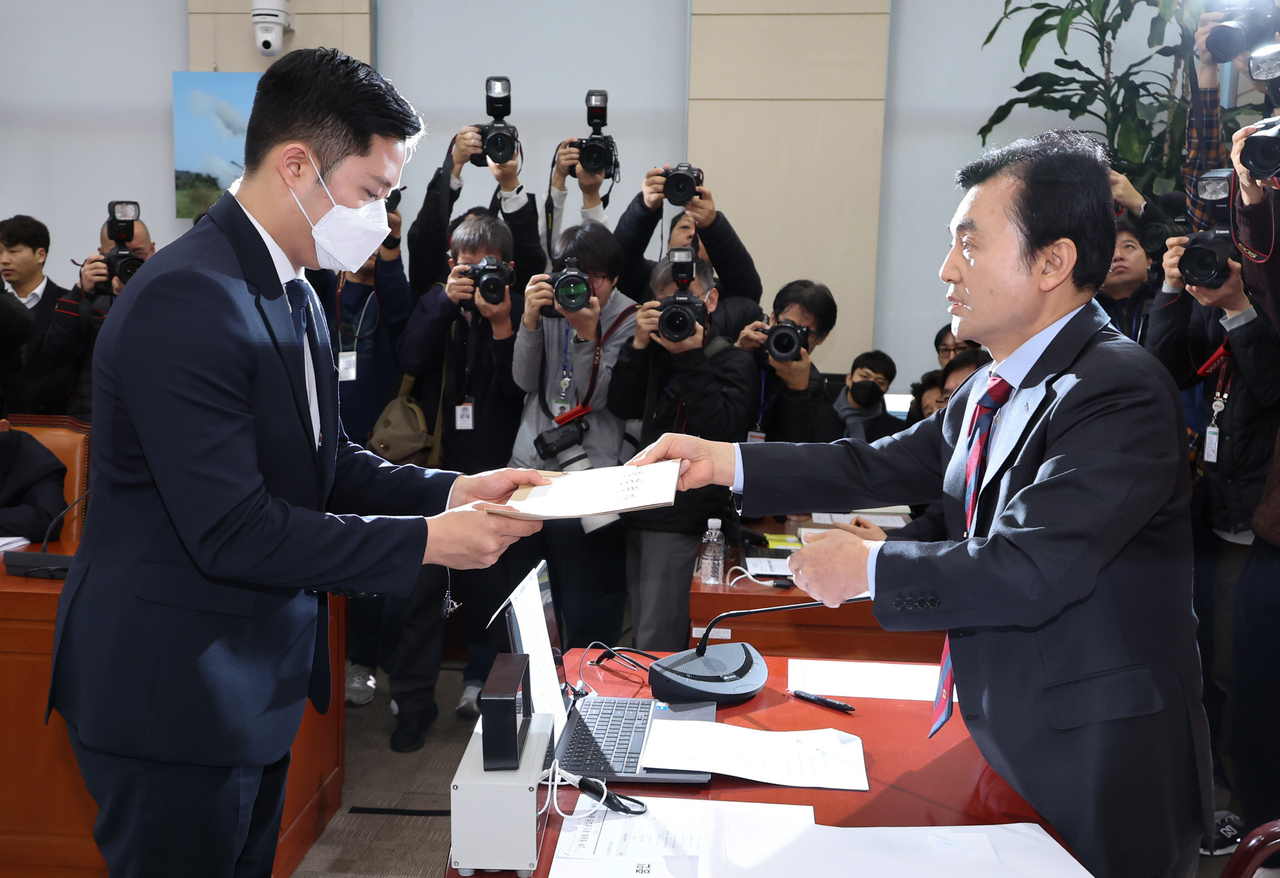 Rep. Ahn Gyu-back (right), chair of the special committee investigating President Yoon Suk Yeol's insurrection charges, hands over a document to a parliamentary official after issuing orders to bring former Defense Minister Kim Yong-hyun and three others involved in Yoon's martial law declaration to appear at the National Assembly as witnesses on Tuesday. (Yonhap)