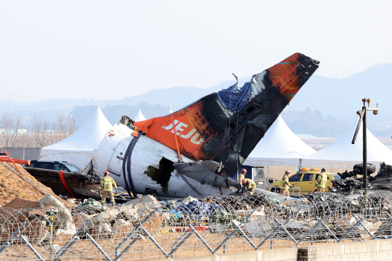 Firefighters remove tarpaulin sheets covering the debris of a Jeju Air passenger plane at Muan International Airport, southwestern South Korea on Jan. 13, following its crash on Dec. 29. (Yonhap)