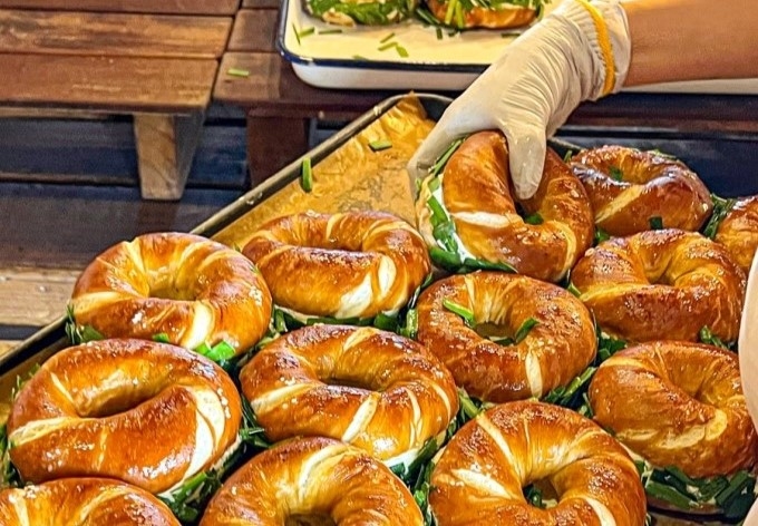 A London Bagel Museum staff member holds up a bagel sandwich from a tray. (London Bagel Museum Instagram)