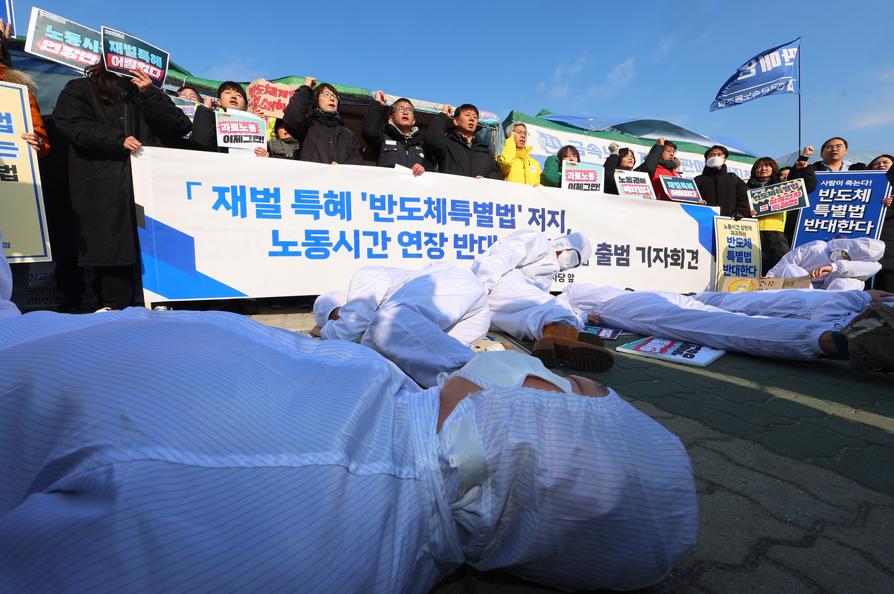 Protesters in protective suits stage a performance symbolizing overworked semiconductor workers collapsing from exhaustion during a press conference outside the National Assembly in Seoul on Feb. 10. The demonstration, organized by labor unions, the Justice Party, and civic groups, opposed the K-Chips Act, arguing it would extend working hours and worsen environmental issues. (Yonhap)