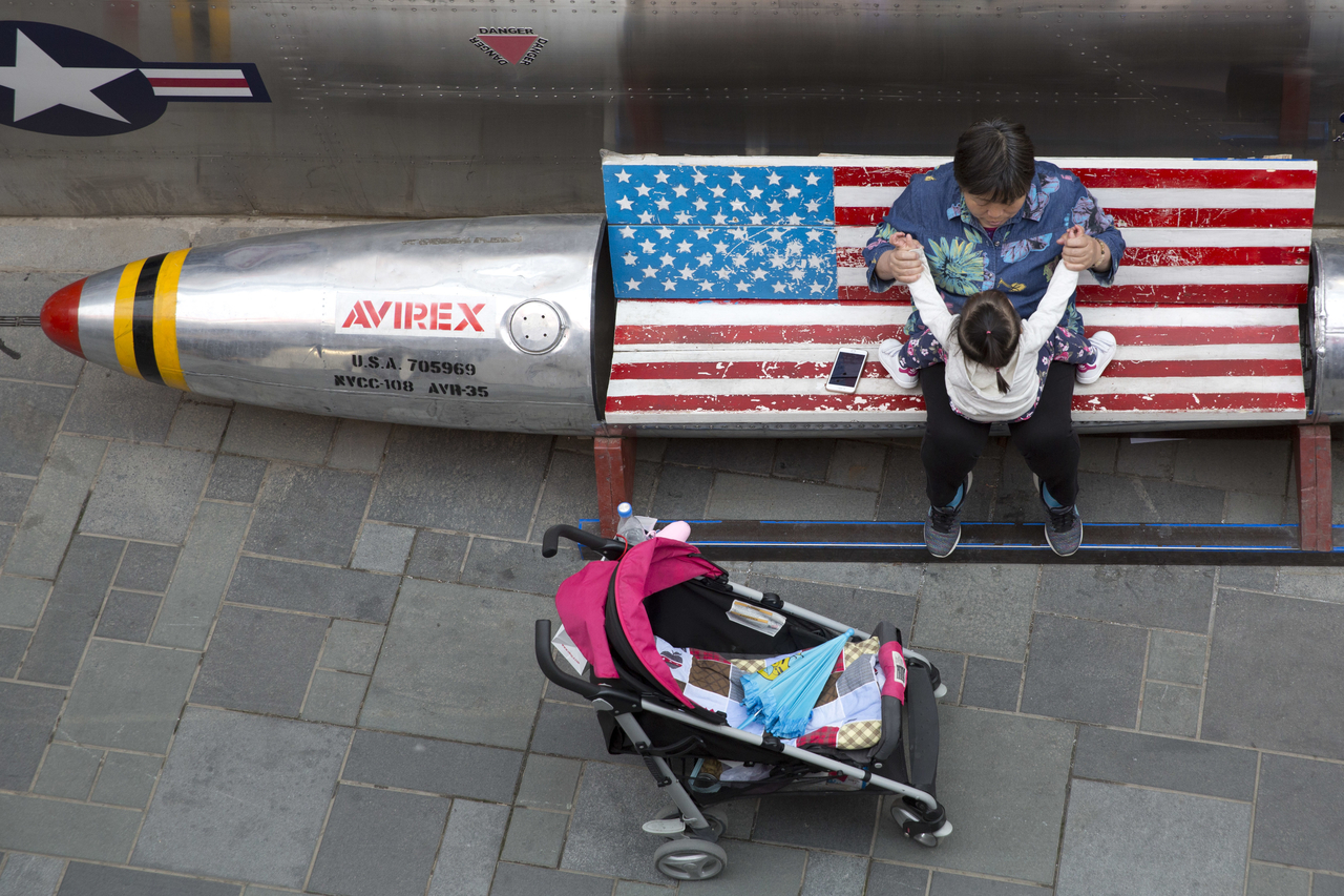 A woman tends to a child near a promotional gimmick in the form of a bomb and the U.S. flag outside a U.S. apparel shop in Beijing on April 12, 2018. [AP]