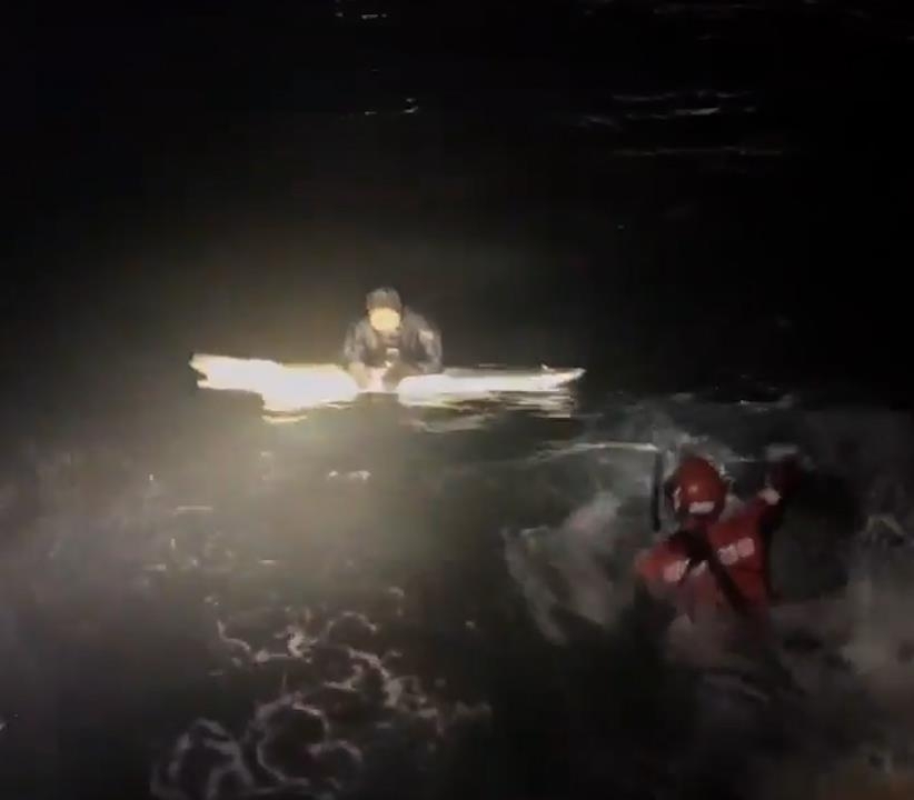 A diver is seen clinging to a broken surfboard as a rescue worker approaches. (Yonhap)