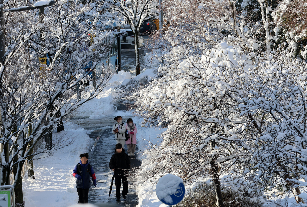Elementary school students head to school in Gyo-dong, Gangneung, after heavy snowfall on Monday. (Yonhap)