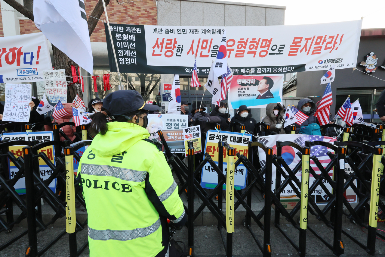 A police officer confronts protesters calling on the Constitutional Court to overturn the parliament's motion to impeach President Yoon Suk Yeol near the Constitutional Court on Friday. (Yonhap)