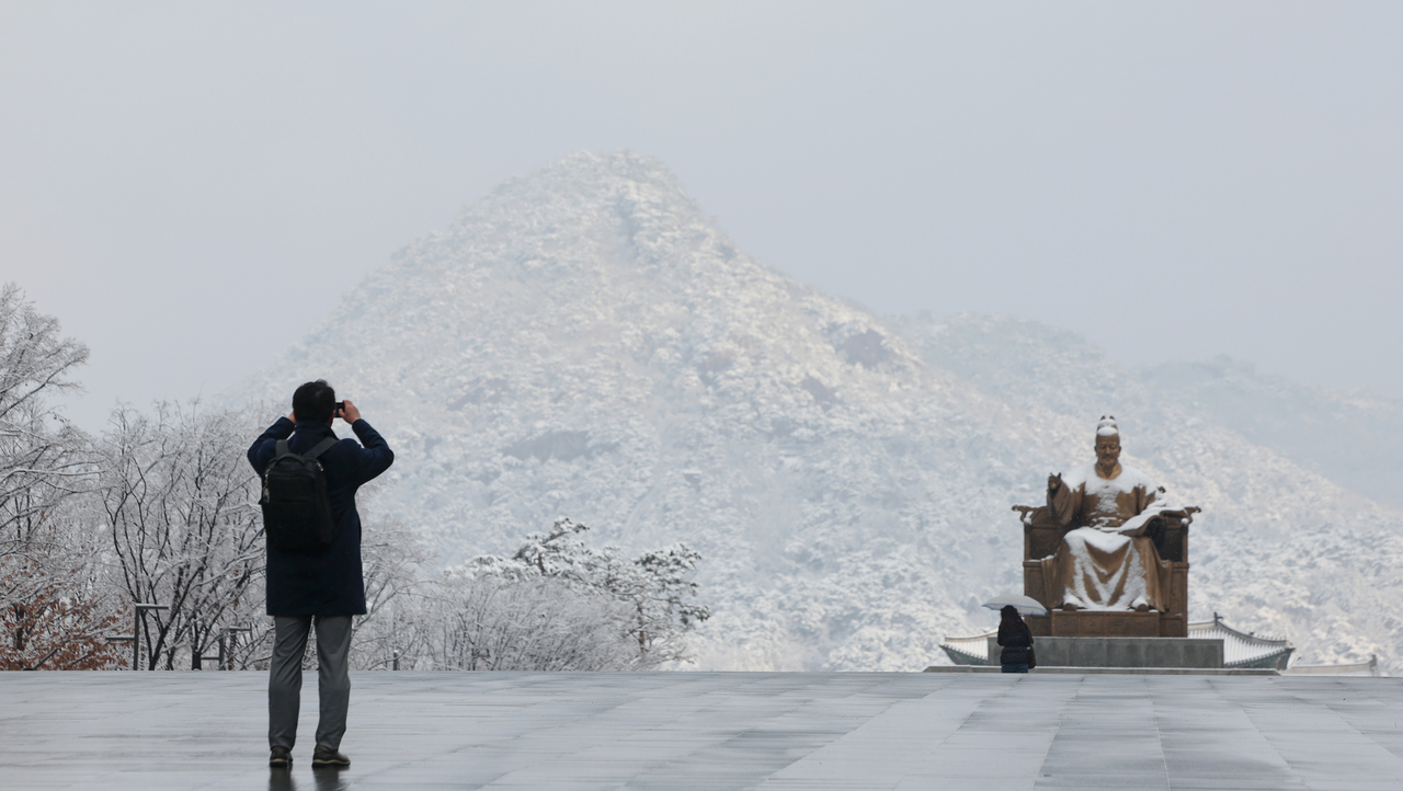 A pedestrian snaps a photo of the statue of King Sejong in Gwanghwamun Square in Jongno-gu, central Seoul, Tuesday, the same day a heavy snow warning was issued in the city. Tuesday’s heavy snow warning was the latest heavy snow warning the city had issued on record, dating to 1999. (Yonhap)