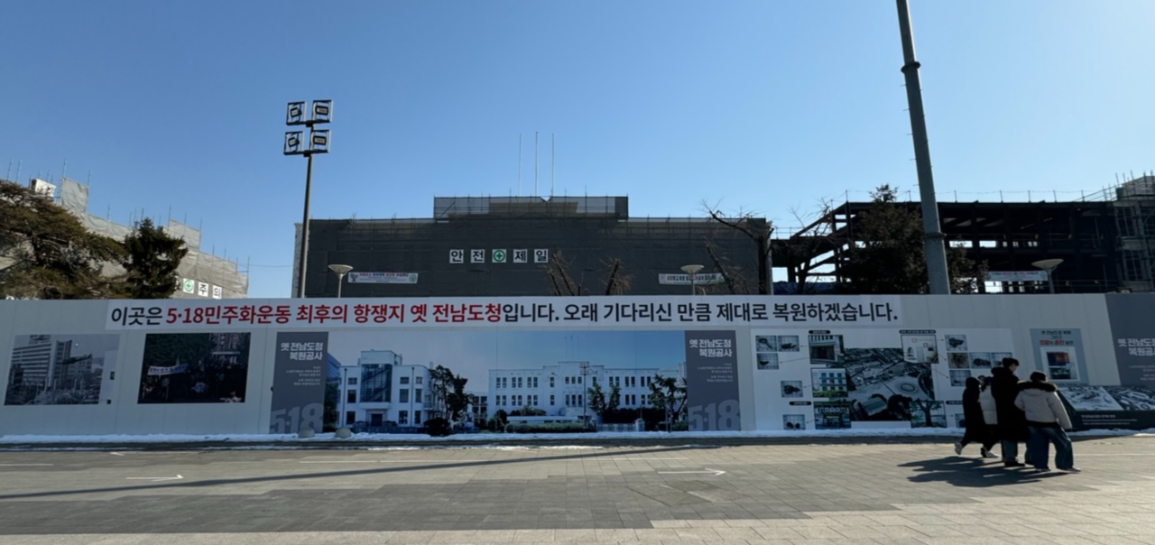 People walk past the restoration site of the former South Jeolla Provincial Office in Gwangju on Feb. 12. The sign reads "This is the former South Jeolla Provincial Office, the final stronghold of the May 18 Democratic Uprising. We will ensure a proper restoration, as you have waited a long time." (Park Ga-young/The Korea Herald)