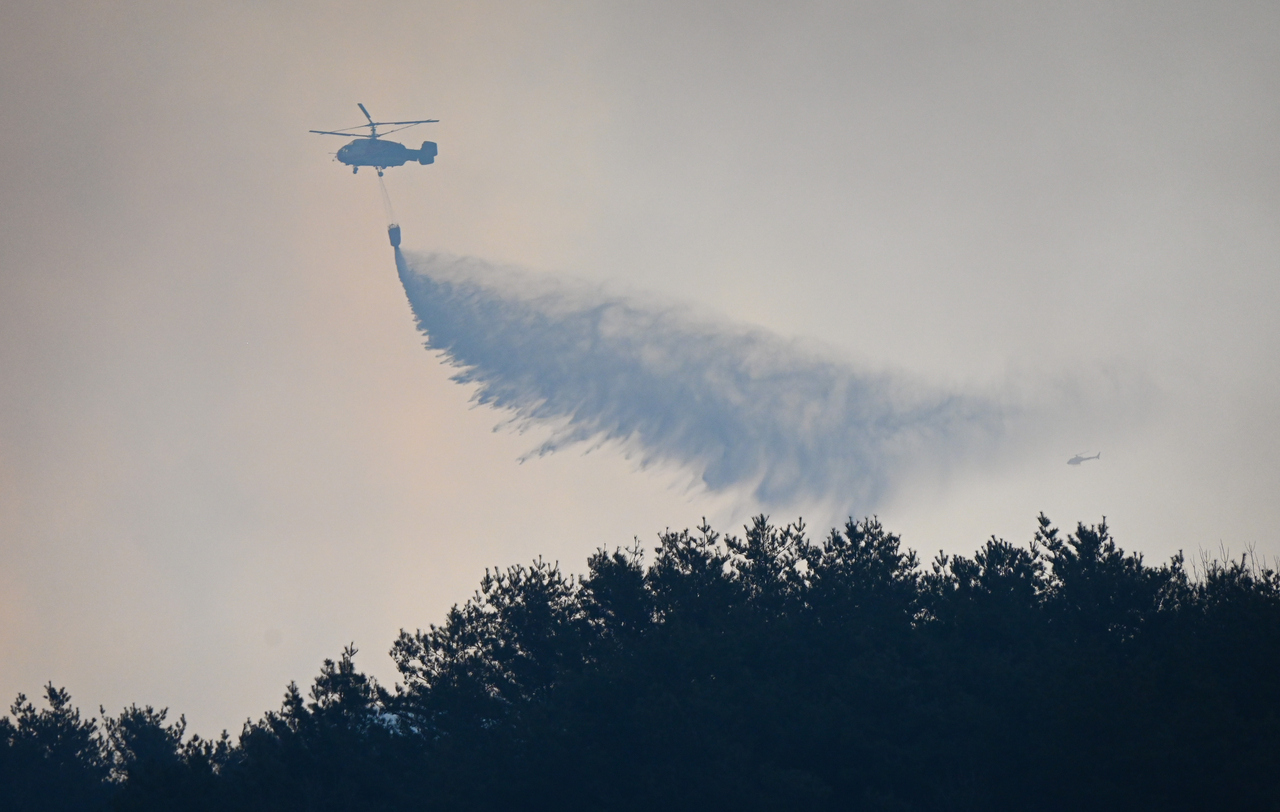 Authorities put out a fire using a helicopter on Saturday, a day after a wildfire broke out in the southeastern county of Sancheong, in this photo provided by the South Gyeongsang provincial government. (Yonhap)