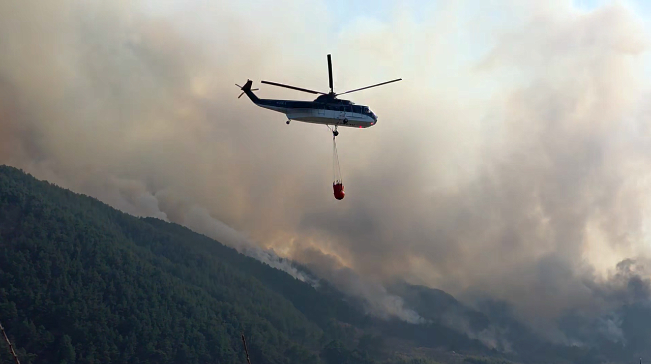 Authorities put out a fire using a helicopter on Saturday, a day after a wildfire broke out in the southeastern county of Sancheong. (Yonhap)