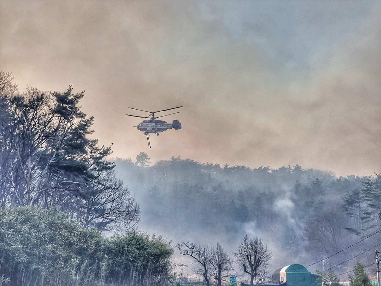 Authorities put out a fire using a helicopter on Sunday, a day after a wildfire broke out in the southeastern county of Sancheong, in this photo. (South Gyeongsang provincial government)