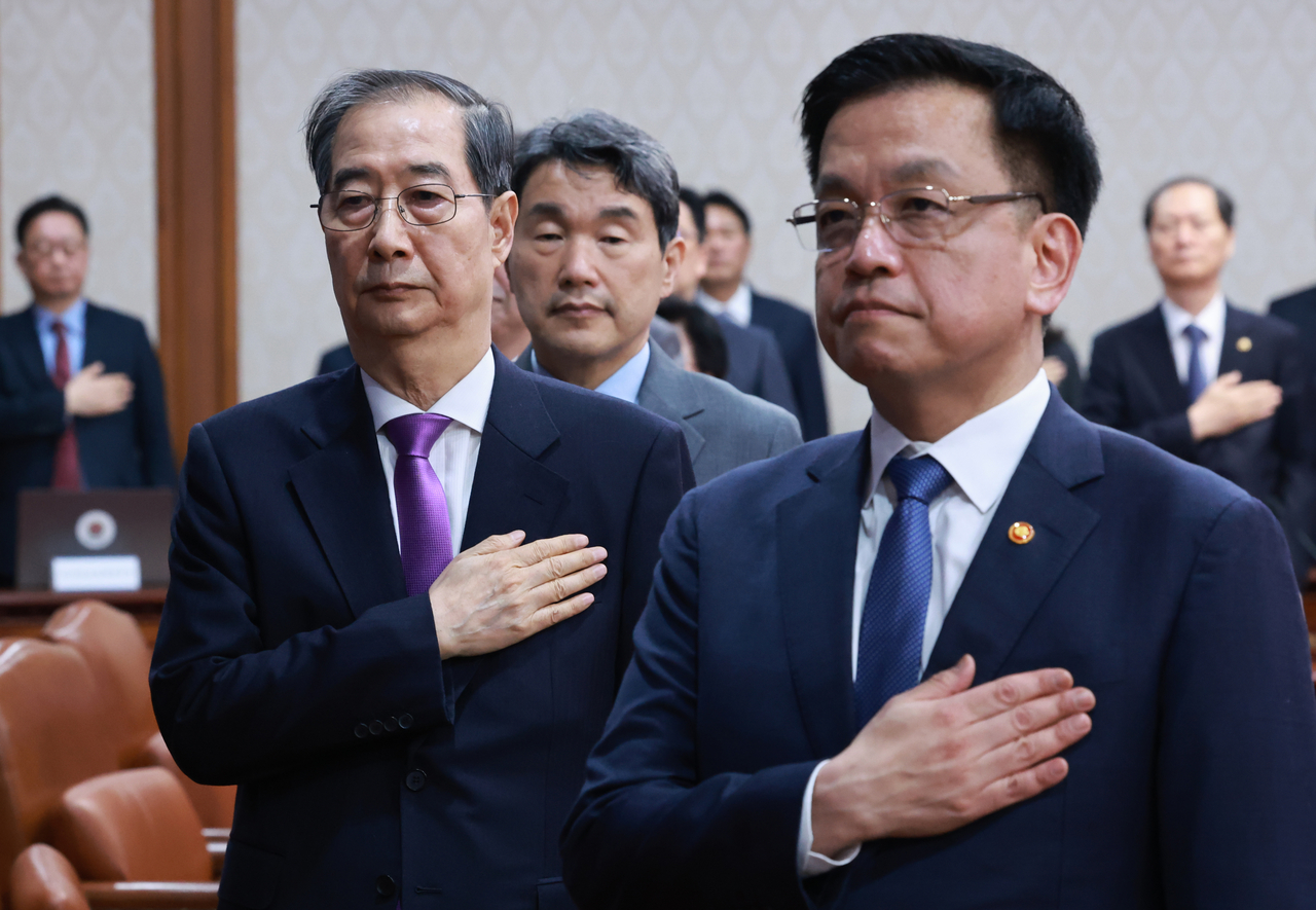 Prime Minister and Acting President Han Duck-soo (left) and Deputy Prime Minister and Finance Minister Choi Sang-mok (right) and other members of the Cabinet salute the national flag at a Cabinet meeting held at the Government Complex Seoul on Tuesday. (Yonhap)