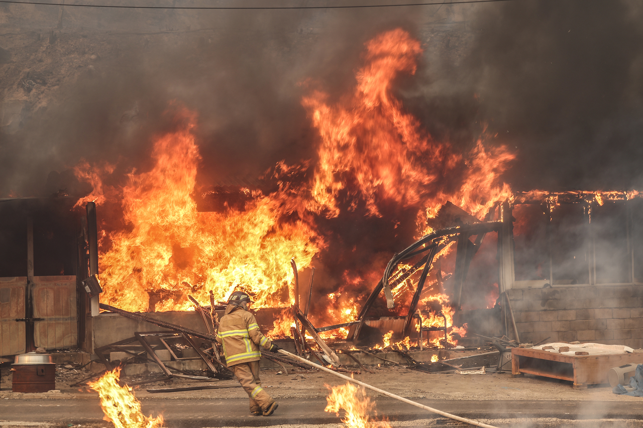 A firefighter pulls a hose toward a burning structure in Hahwa 1-ri, Danchon-myeon, Uiseong-gun, Tuesday, as embers from the ongoing wildfire ignite secondary fires in the area. (Yonhap)