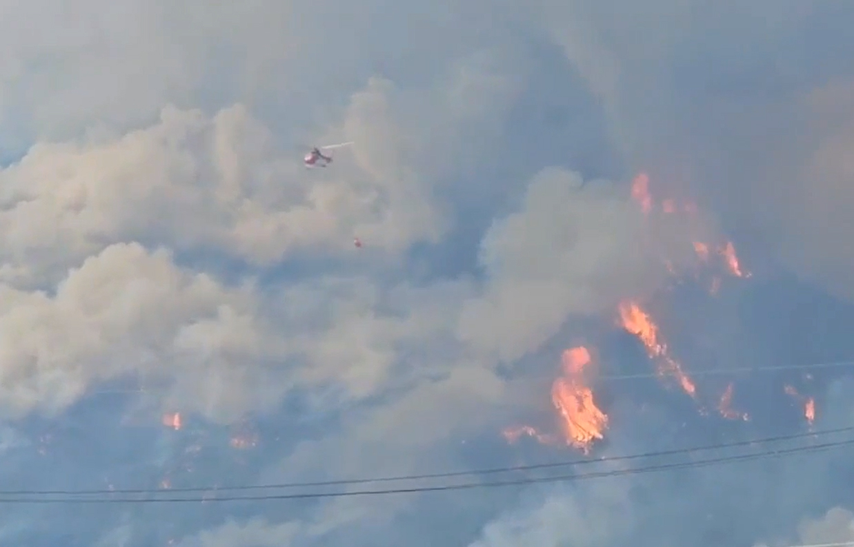 Amid heavy smoke, a firefighting helicopter works to contain a wildfire burning across mountainous slopes in Sancheong-gun, South Gyeongsang, on Saturday.
