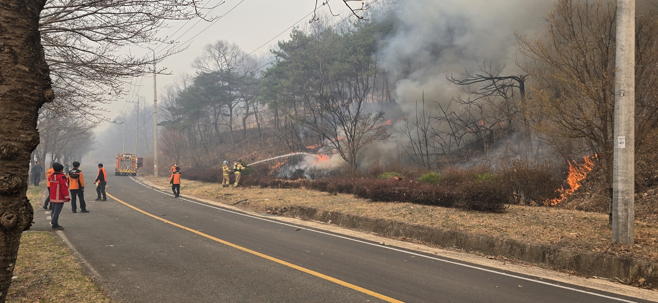 Firefighters work to contain a wildfire on Wednesday afternoon in Sinpyeong-myeon, Uiseong, after an S-76 helicopter leased from Inje, Gangwon Province, crashed during aerial firefighting operations. (Yonhap)