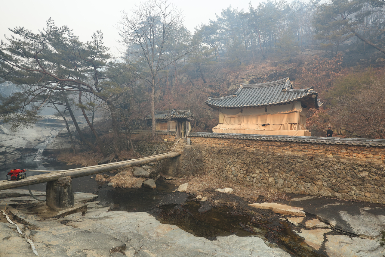 Manhyujeong in Andong, North Gyeongsang Province, stands wrapped in fire-retardant cloth Wednesday, a day after it survived a ravaging wildfire. (Yonhap)