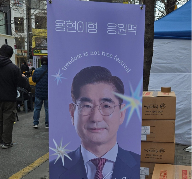 29일 서울 서대문구 신촌역 일대에서 ‘탄핵을 반대하는 대한민국 청년’ 등 주최로 열린 자유 토크쇼에 김용현 전 국방부 장관이 떡을 돌렸다는 내용의 입간판이 설치된 모습. [엑스(X) 캡처]