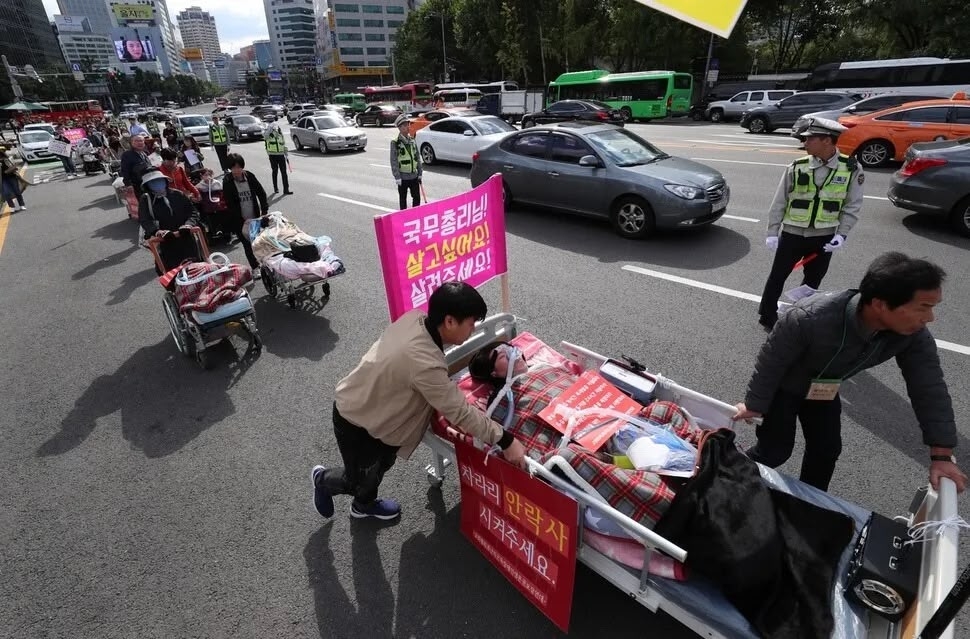Jang Ik-seon, alongside fellow activists from the Korean Alliance for the Right to Life of People with Muscular Disabilities, joins a historic protest on Oct. 10, 2018, marching on hospital beds and wheelchairs through Seoul to demand 24-hour personal assistance, a necessity for their survival. (The Korean Alliance for the Right to Life of People with Muscular Disabilities)