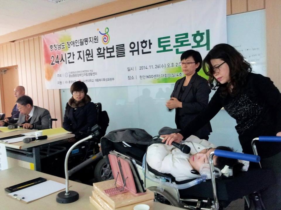 Jang Ik-seon, then serving as president of the Gwangju Muscular Dystrophy Association, delivers a speech at the 2014 South Chungcheong Province Forum on Securing 24-Hour Support for People with Disabilities, urging policy reforms for continuous care. (Courtesy of Jang Ik-seon)