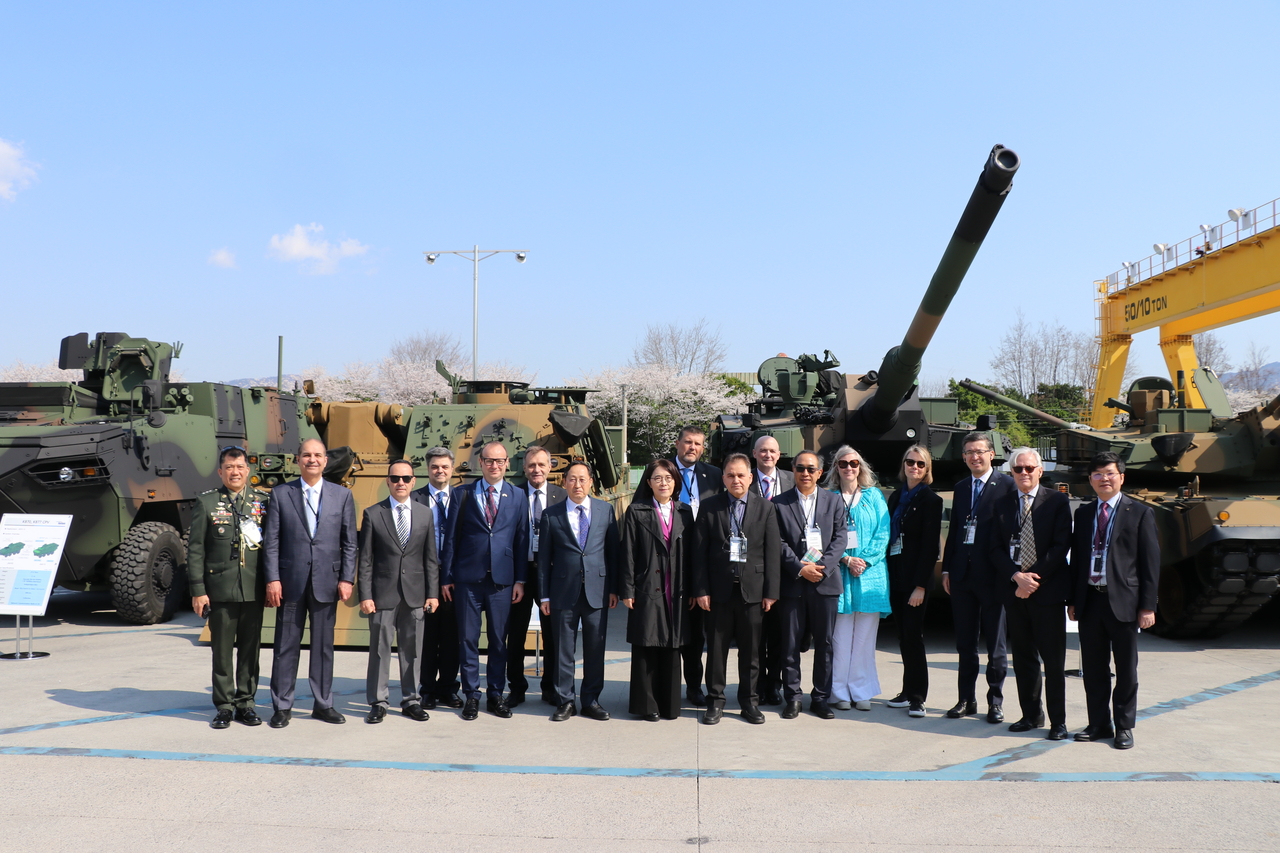The diplomatic corps from 15 countries take a group photo in front of the K-2 Black Panther tank and its variables at Hyundai Rotem in Changwon, South Gyeongsang Province, Wednesday. (Republic of Korea Ministry of Foreign Affairs via Hyundai Rotem)
