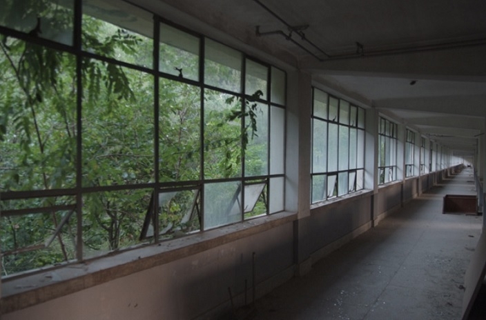 A dimly lit hallway with shattered windows and a worn floor at the abandoned Chungil Girls' High School (Yuseong-gu Office)