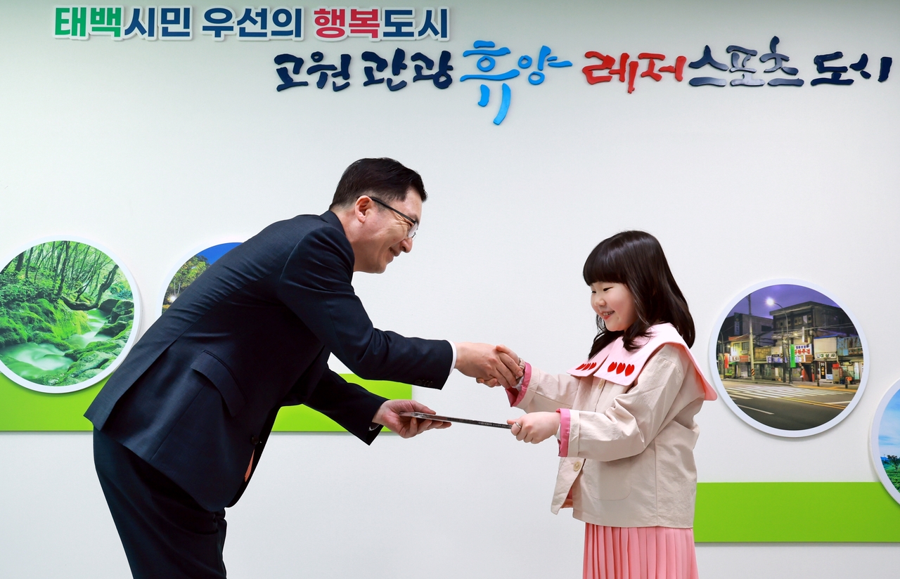 나채범(왼쪽) 한화손해보험 대표가 8일 오후 태백시청에서 열린 ‘지역활성화를 위한 동화책 기증식’에서 태백시 홍보 아역배우 유슬 양에게 창작 동화 ‘땅요가 알려주는 석탄 이야기’를 전달하며 기념촬영을 하고 있다. [한화손해보험 제공]