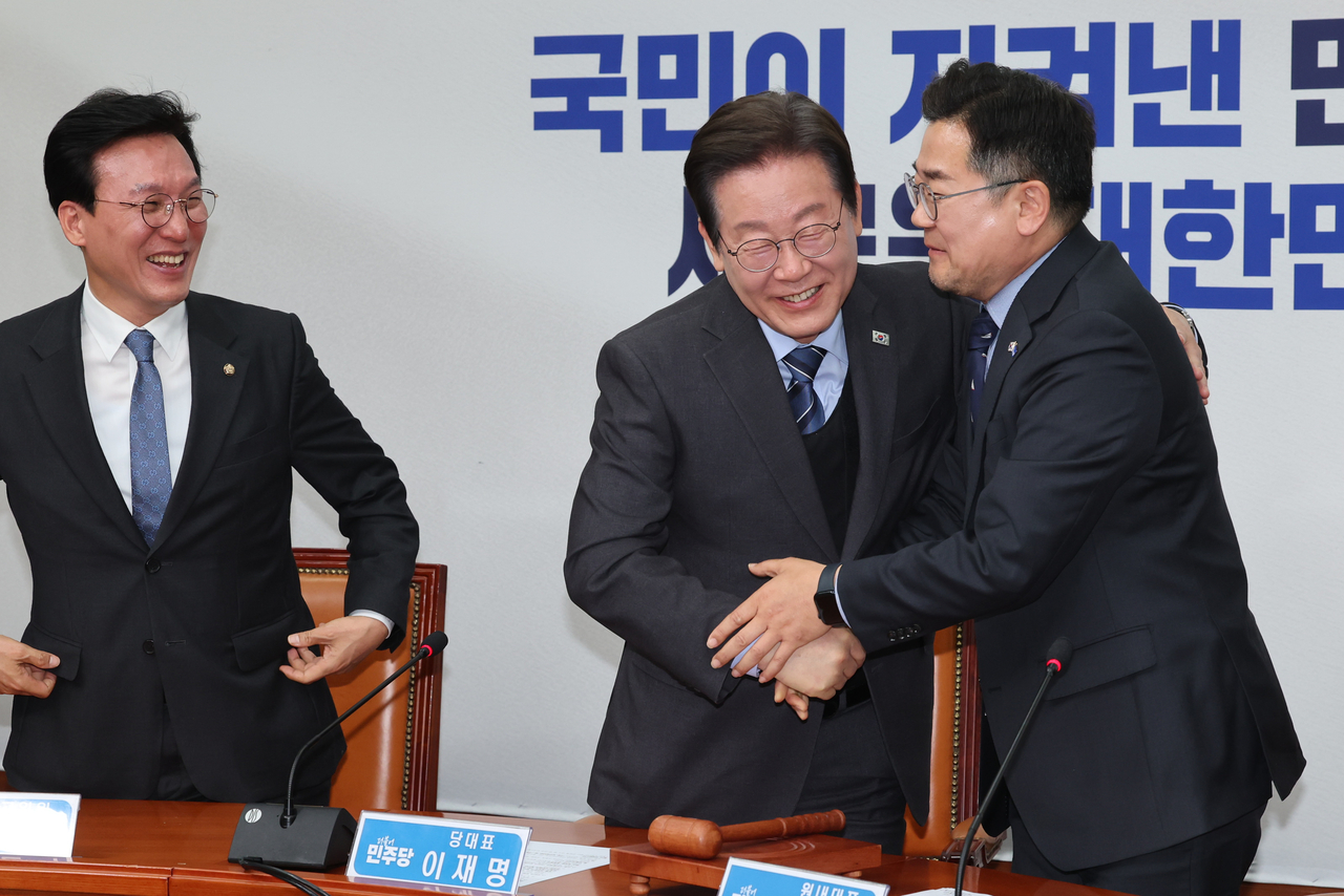 Main opposition Democratic Party of Korea Chair Rep. Lee Jae-myung (center) shakes hands with Rep. Park Chan-dae, the party's floor leader, after resigning as party chair during the party's Supreme Council meeting held at the National Assembly on Wednesday. (Yonhap)