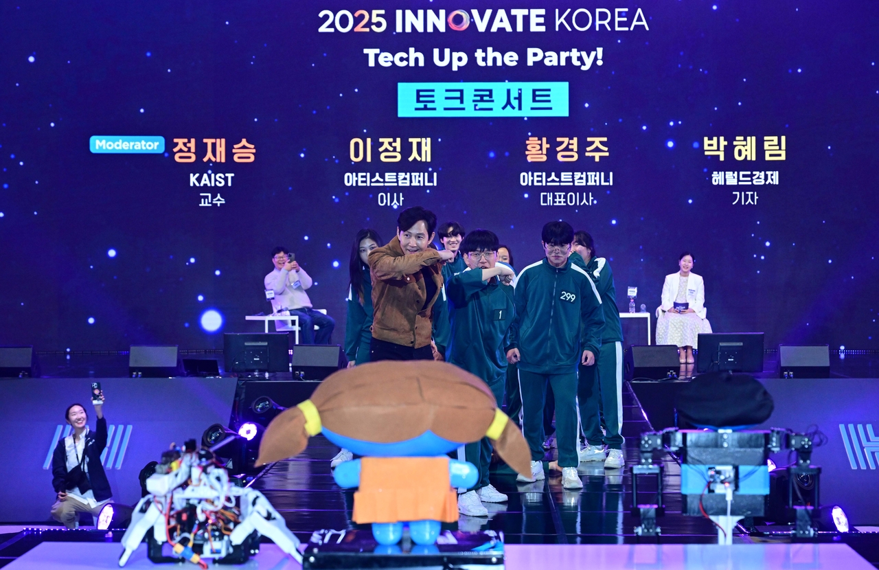 Actor Lee Jung-jae reenacts a scene from Netflix's "Squid Game" with members of KAIST's robotics club, at the Innovate Korea 2025 forum held on the KAIST campus on Wednesday. (Lee Sang-sub/The Korea Herald)