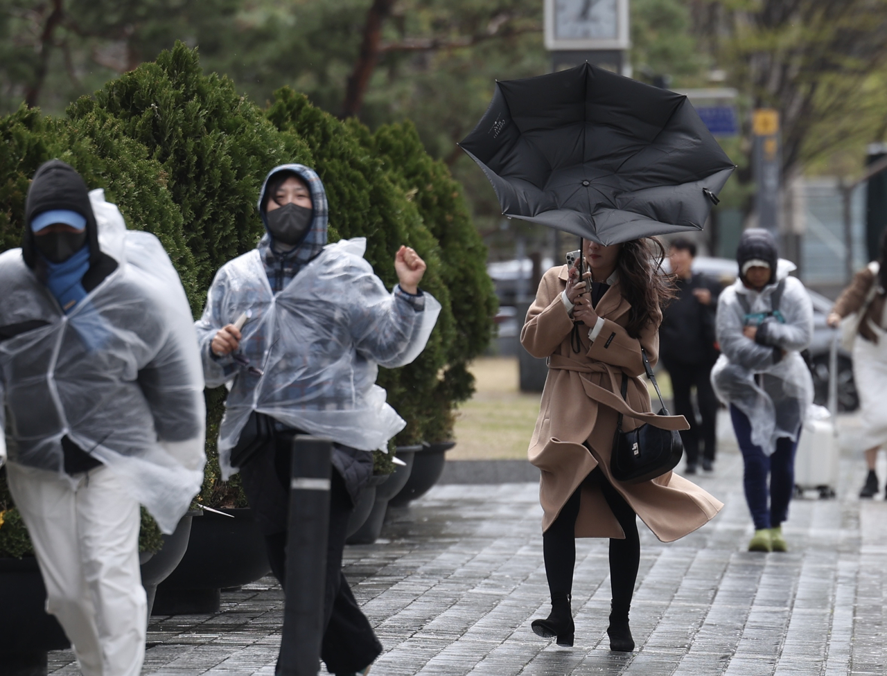 Pedestrians brace themselves against the strong winds and hail that swept through Seoul on Sunday. (Newsis)