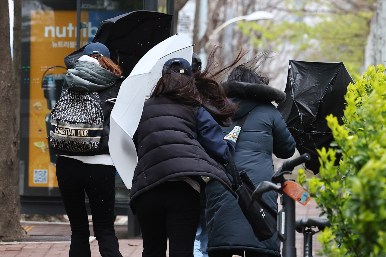 Pedestrians grapple with their umbrellas as strong winds and hail batter Seocho-gu, Seoul, on Sunday. (Yonhap)