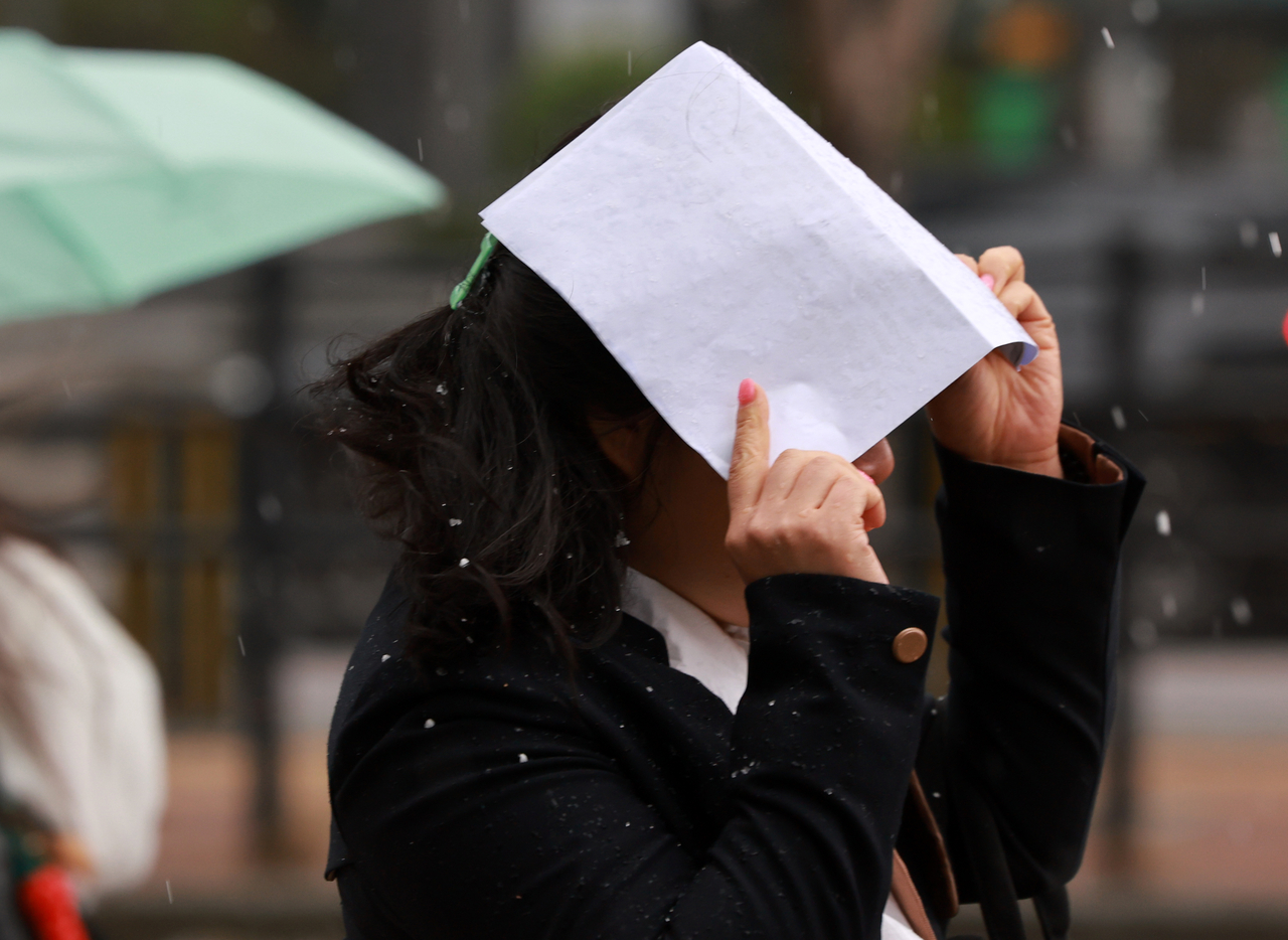 A woman covers her head with a piece of paper as strong winds and hail sweep through Seoul on Sunday. (Yonhap)