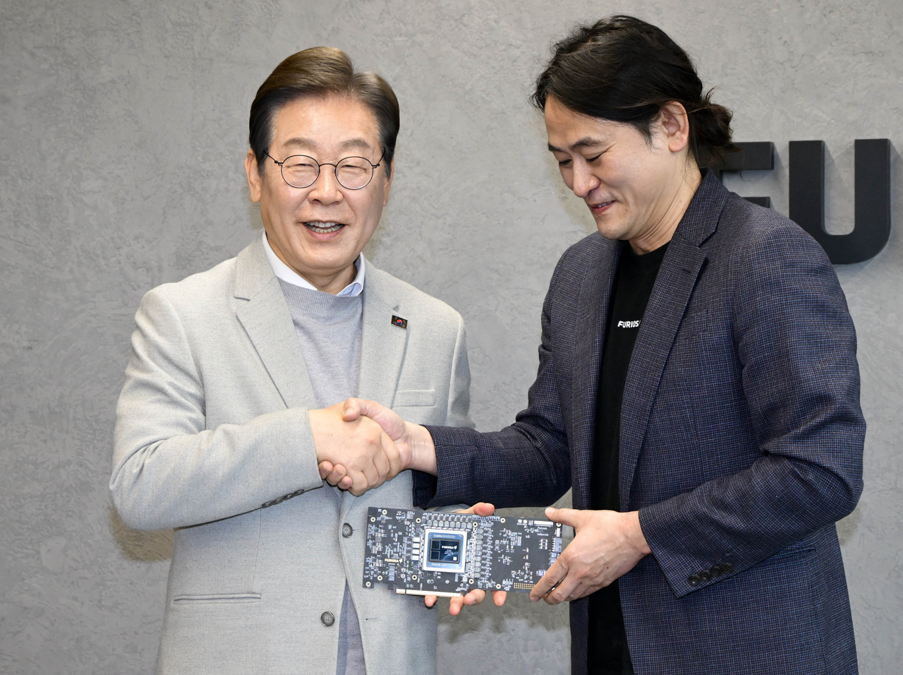 Rep. Lee Jae-myung (left), former leader of the main opposition Democratic Party of Korea, shakes hands with FuriosaAI CEO Paik June at the company's headquarters in Gangnam-gu, southern Seoul, Monday. (Pool photo via Yonhap)