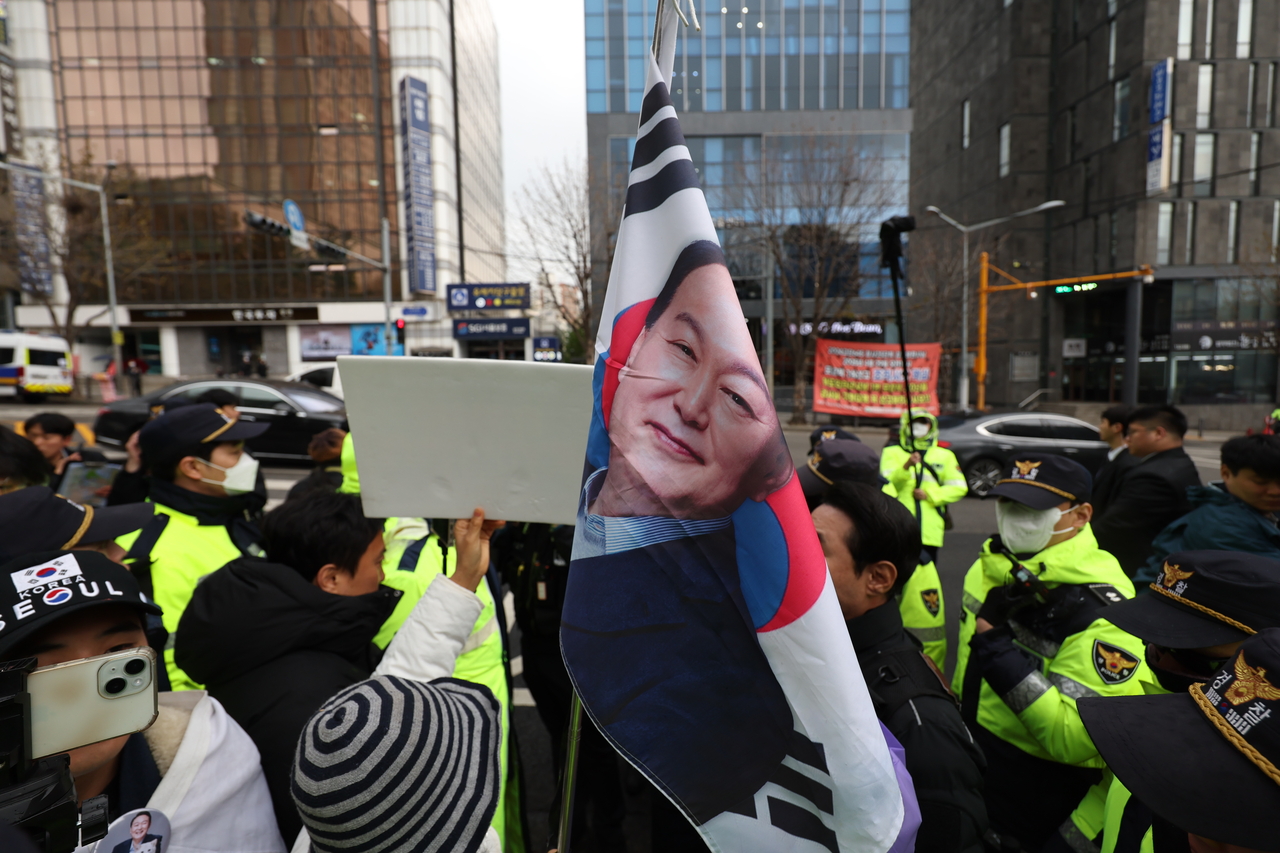 A protester is seen holding the South Korean flag with a portrait of former President Yoon Suk Yeol edited into it, in support of Yoon in front of Seoul Central District Court on Monday, as Yoon’s criminal trial on charges of orchestrating an insurrection through declaring martial law Dec. 3 was taking place. (Yonhap)