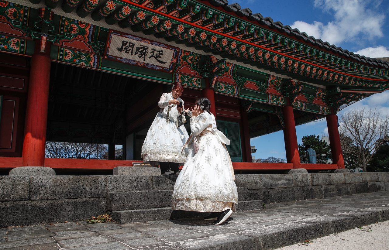 Foreign tourists dressed in Korean traditional attire, hanbok, take photos at Gwandeokjeong on Jeju Island on March 17, a filming location featured in the hit Netflix series "When Life Gives You Tangerines." (Newsis)