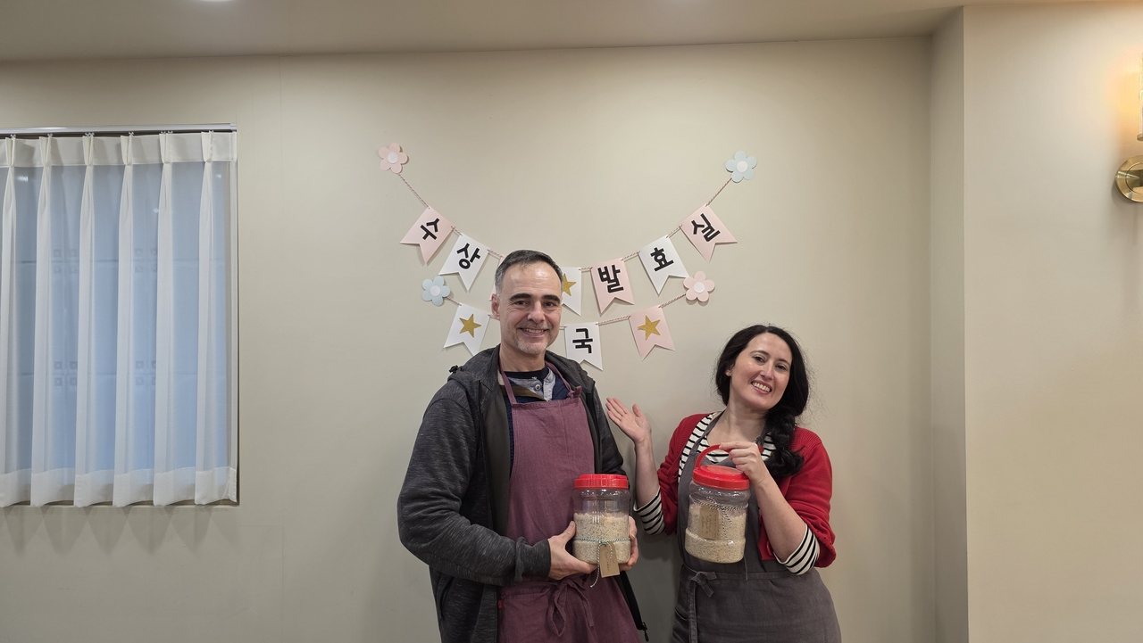 From left: Gilles and Laure Landric, a couple from France, pose with their fermentation pot filled with makgeolli ingredients at Suguk in Seoul on Monday. (Suguk)