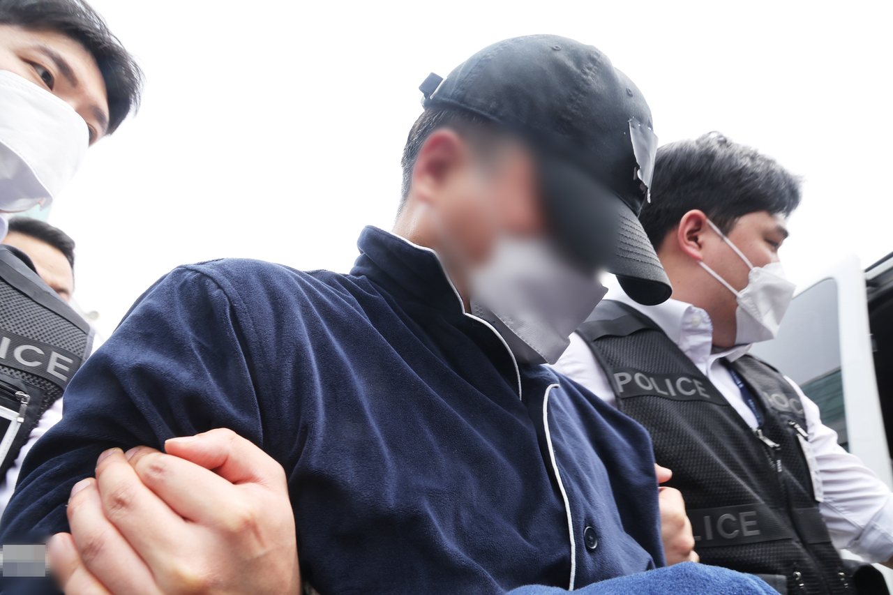 A man in his 50s, suspected of killing his parents, wife and two daughters, is escorted out of the Yongin Seobu Police Station by police officers in Gyeonggi Province, Thursday. (Yonhap)
