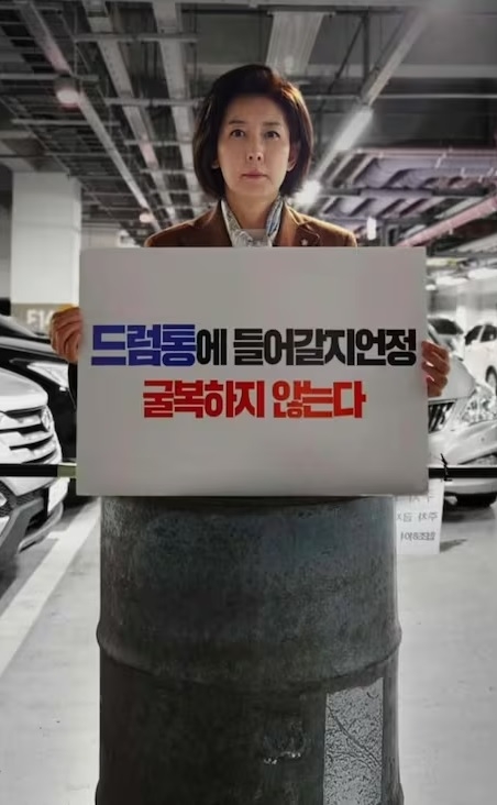 Na poses standing in a steel barrel holding a sign that says, “I’d rather get into a drum barrel than surrender.” (Na’s Facebook page)