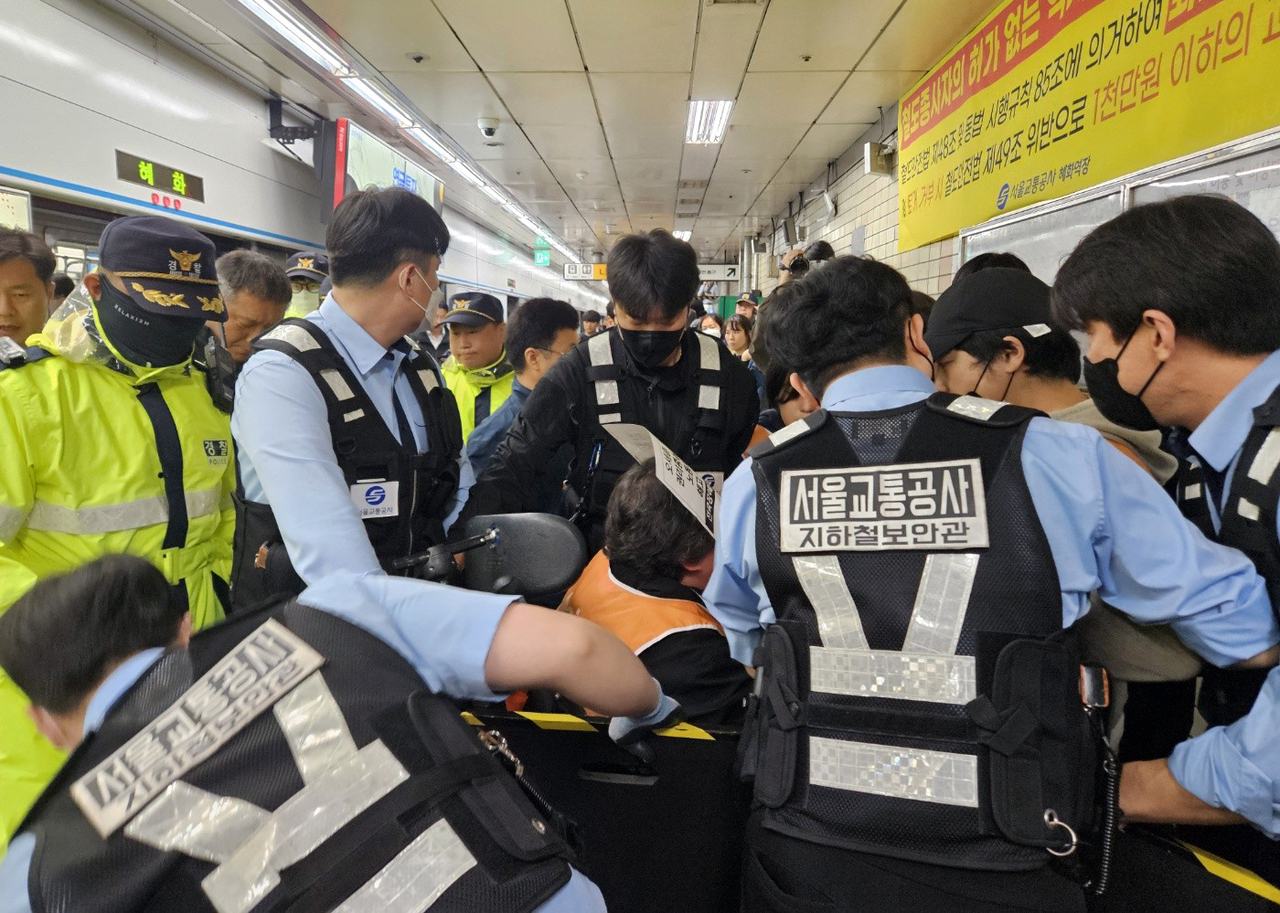 Seoul Metro subway security officers try to force a wheelchair-bound protester out of Hyehwa Station in central Seoul on Tuesday. (Yonhap)