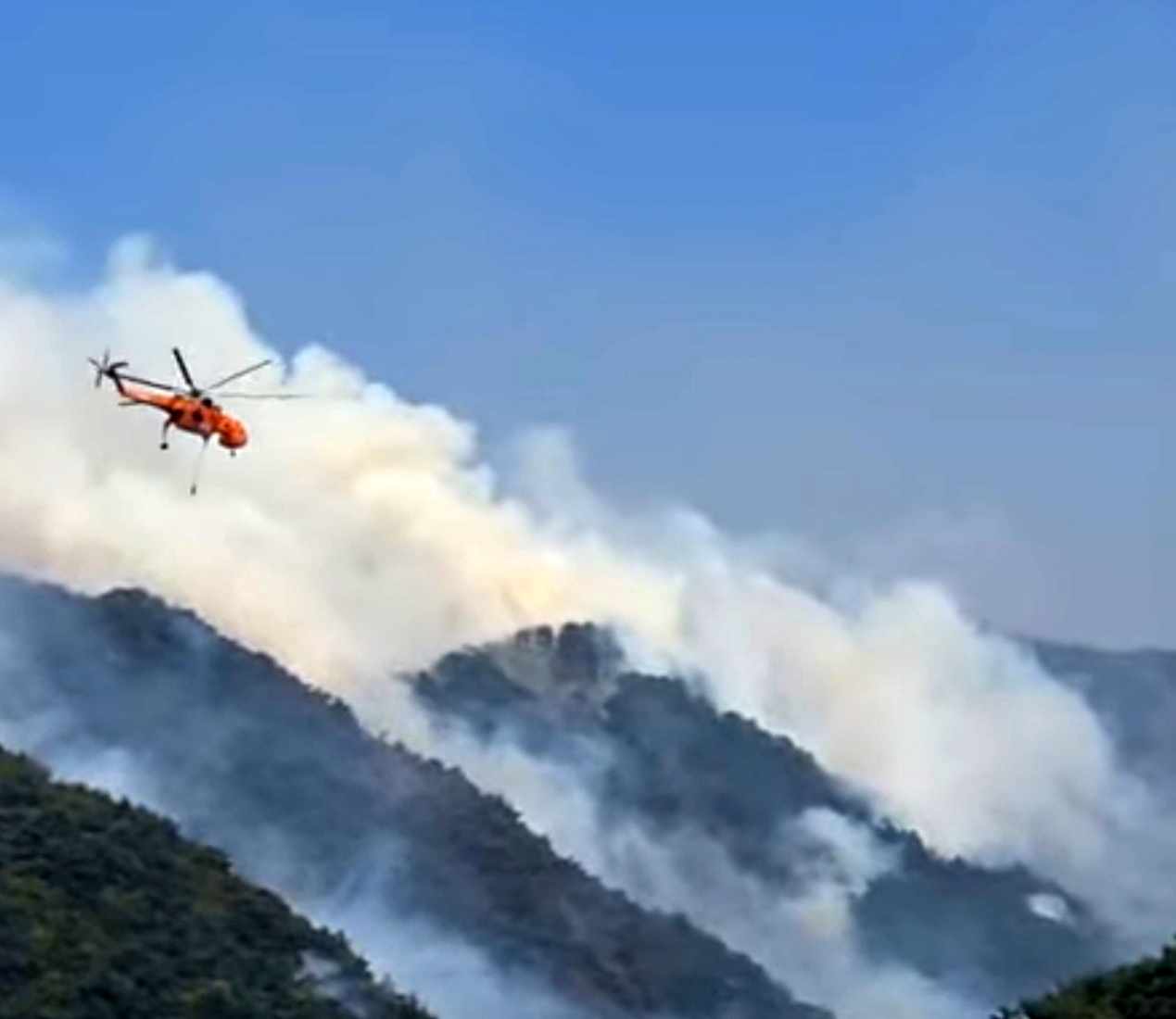 A Korea Forest Service helicopter battles a spreading wildfire in a mountainous area near Inje County on Saturday afternoon. (Yonhap)