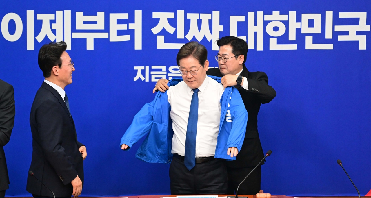 박찬대 더불어민주당 직무대행 겸 원내대표가 28일 서울 여의도 국회에서 열린 최고위원회의에서 이재명 대선 후보에게 선거운동용 파란색 점퍼를 입혀주고 있다. 이상섭 기자