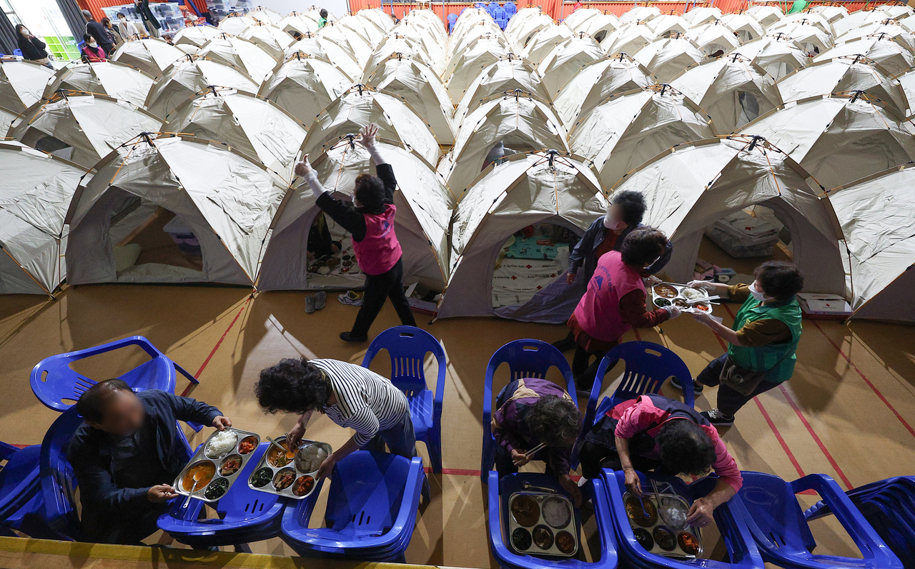 Daegu residents at a temporary shelter are served breakfast, using chairs as makeshift tables, Tuesday morning. (Yonhap)