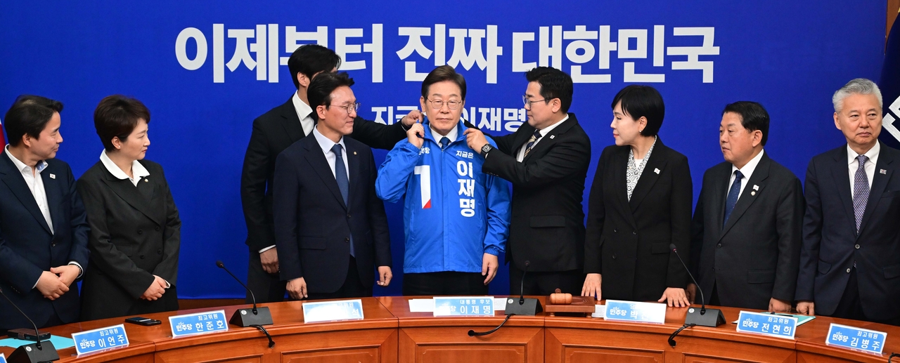 박찬대 더불어민주당 직무대행 겸 원내대표가 28일 서울 여의도 국회에서 열린 최고위원회의에서 이재명 대선 후보에게 선거운동용 파란색 점퍼를 입혀주고 있다. 이상섭 기자