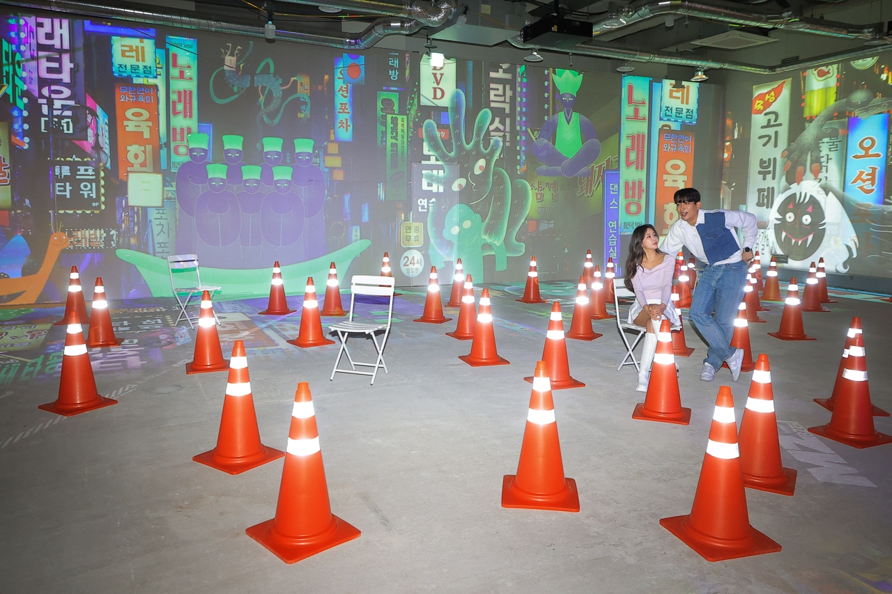A concrete room is filled with traffic cones and surreal projections of city monsters and neon signage. (Yonhap)