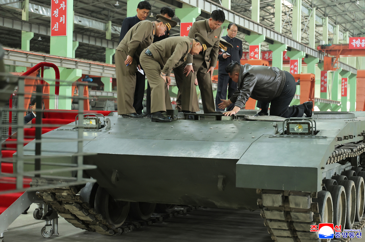 North Korean leader Kim Jong-un (right) inspects a tank on his knees inside a factory in this undated photo released by North Korea's official Korean Central News Agency on  Sunday. (Yonhap)