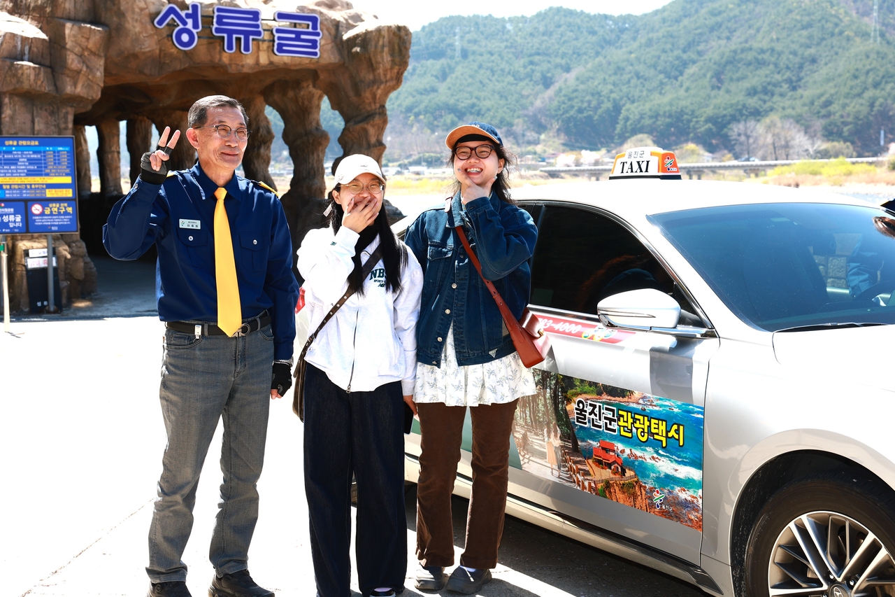 울진 관광택시를 이용한 관광객이 석류굴 앞에서 운전기사와 함께 기념사진을 찍고 있다[울진군 제공]