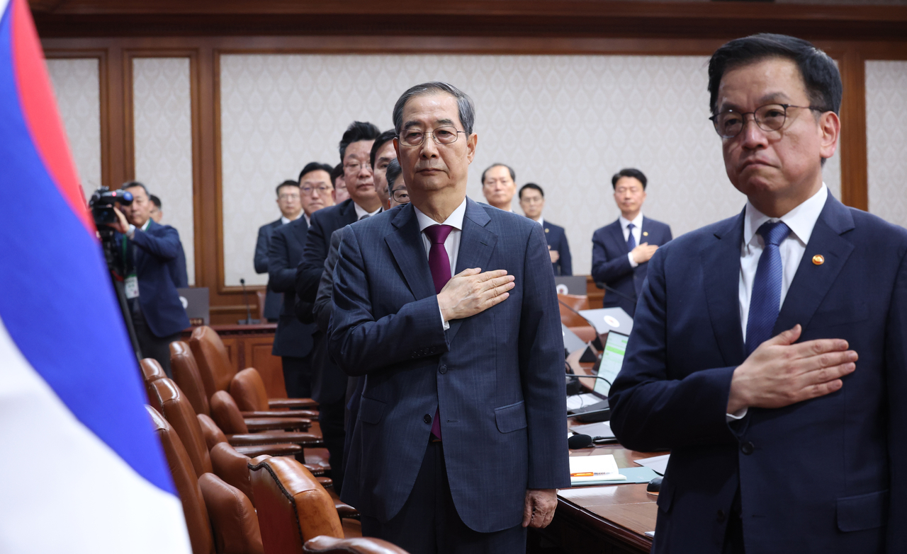 Former Prime Minister Han Duck-soo (left) and former Finance Minister and Deputy Prime Minister Choi Sang-mok are seen saluting the flag during a Cabinet meeting held on April 14. (Newsis)
